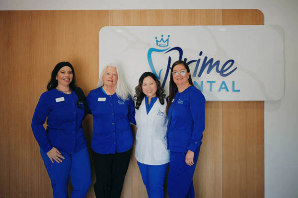 Prime Dental assistant team posing by office sign